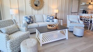 Ein Wohnzimmer mit einer Couch, Sesseln, einem Couchtisch und einem wandmontierten Spiegel.