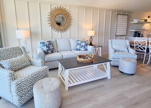 A living room with a sofa, armchairs, a coffee table, and a wall-mounted mirror. - Great Ocean View, Pool, Pickleball & Tennis- Crescent D4B (Pawleys Island)