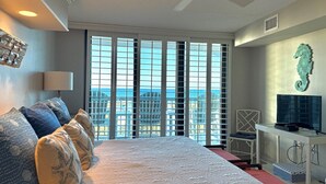 Ein Hotelzimmer mit einem großen Bett, einem Schreibtisch mit Fernseher und Blick auf die Stadt durch raumhohe Fenster.