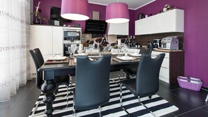 Eine moderne Küche mit Essbereich, mit einem schwarz-weißen Streifen Teppich, schwarzen Stühlen und violetten Pendelleuchten.