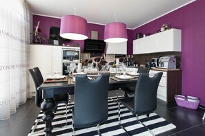 A modern kitchen with a dining area, featuring a black and white striped rug, black chairs, and purple pendant lights. - Exclusive vacation home in Karlshagen with sauna, fireplace & large property (Karlshagen)