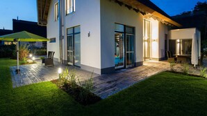Ein modernes Haus mit Terrasse, großen Fenstern und einem Strohdach.
