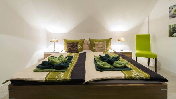 Ein Schlafzimmer mit einem Bett, zwei Nachttischen, einem grünen Sessel und einem Bild an der Wand.
