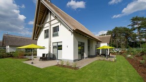 Ein modernes Haus mit Satteldach, zwei großen Fenstern und einer Terrasse mit Sitzgelegenheit.