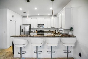 A modern kitchen with white cabinets, a built-in oven, a microwave, and a refrigerator. There are three white bar stools with metal trays. - 1452RFD - Epic 6BR Disney Retreat: Themed Rooms/Spa/Resort Access (Davenport)