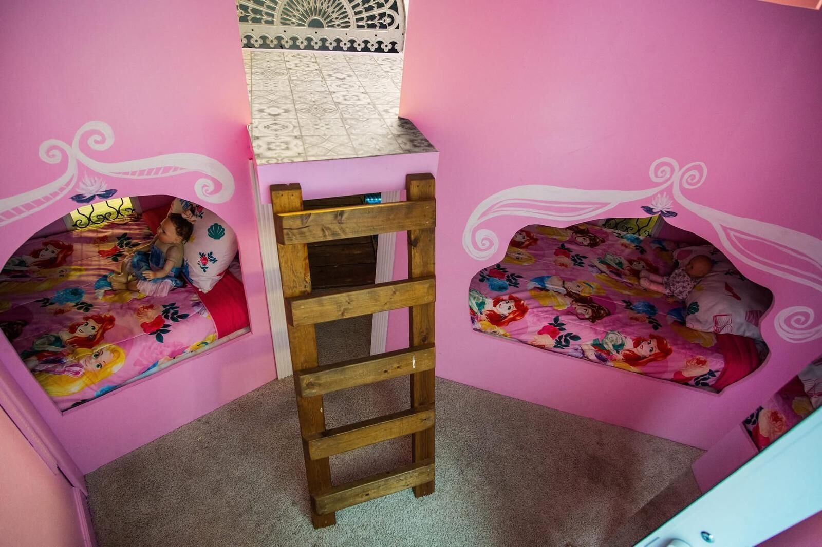 Une chambre rose avec deux lits, chacun recouvert d’une courtepointe à motifs floraux, et une échelle en bois placée au centre.