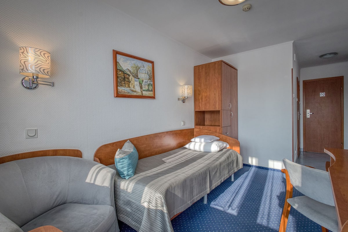 A room with a bed, a chair, a wooden cabinet, and a painting on the wall.