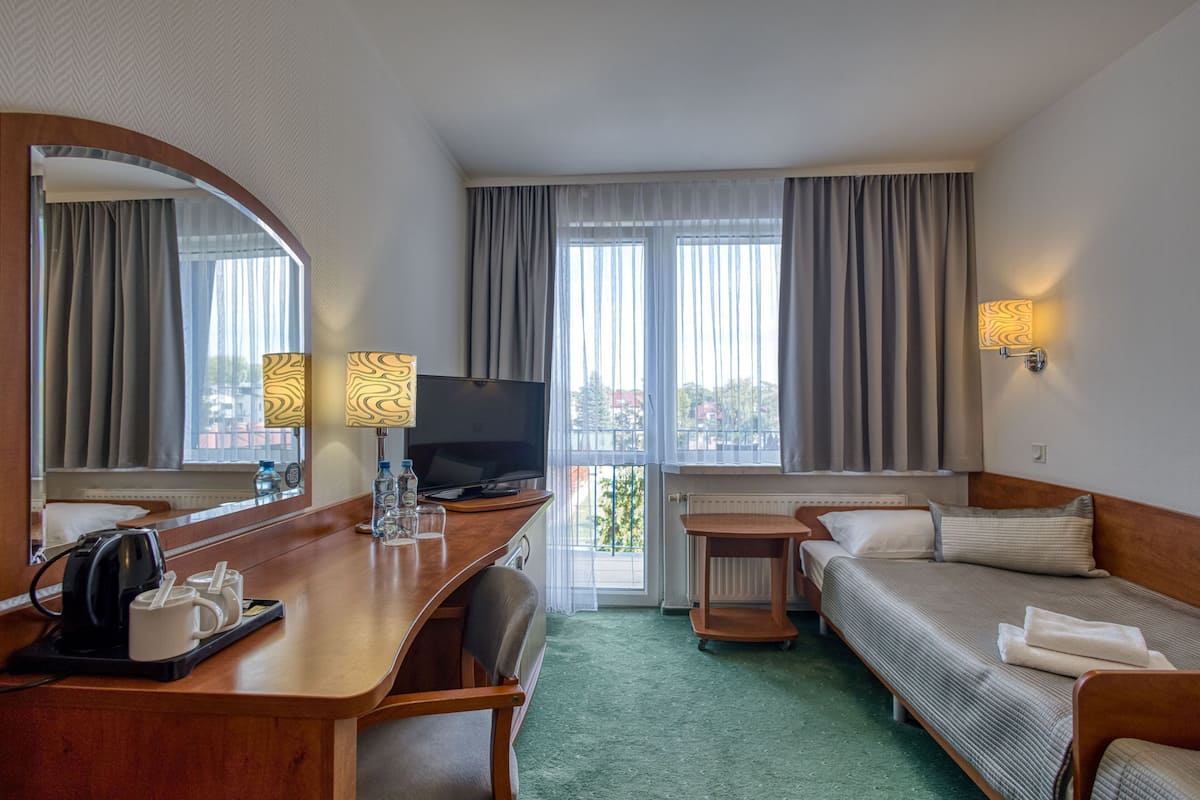 A hotel room with a desk, a television, a sofa, a small table, and a window with curtains.
