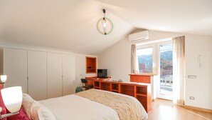 Un dormitorio con cama, escritorio, televisor y ventana con cortinas.