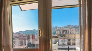 Una habitación con puerta corrediza de vidrio que da a un balcón con vistas a edificios y un paisaje montañoso.