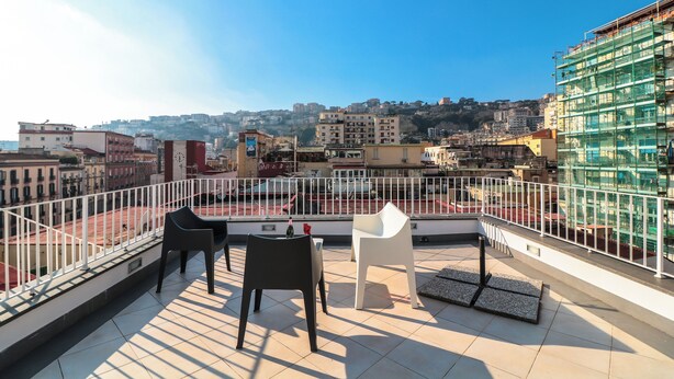 Una terraza en la azotea con dos sillas, una mesita y vistas a un paisaje urbano.