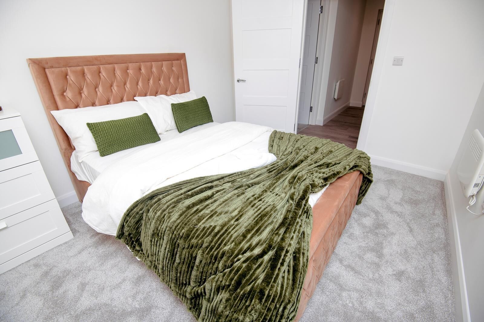 A bedroom with a tufted headboard, white bedding, green pillows, and a green throw blanket.