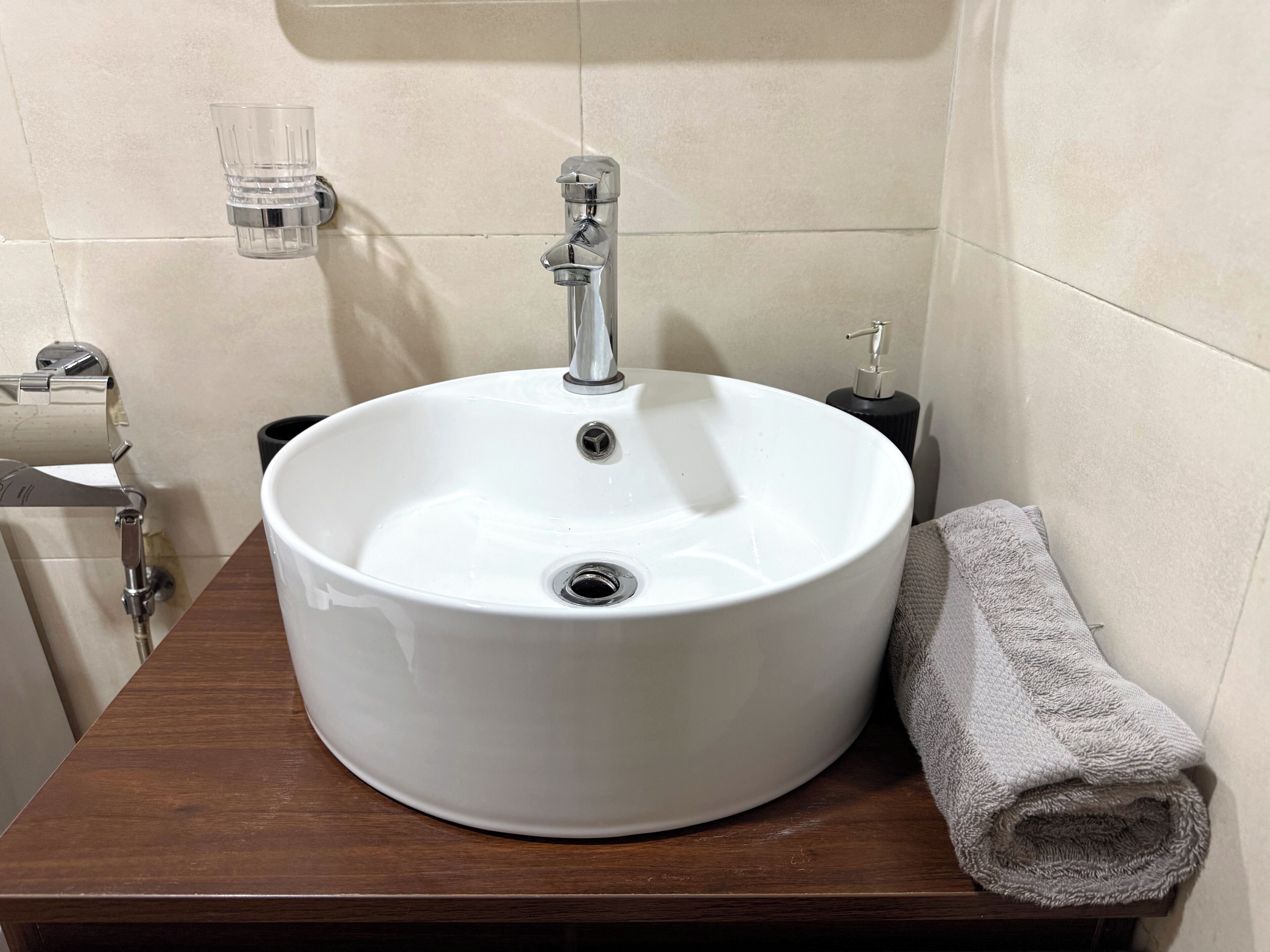 Ein Badezimmer mit einem weißen Waschbecken, einer Holzablage, einem Handtuch und einer Seifenspender.
