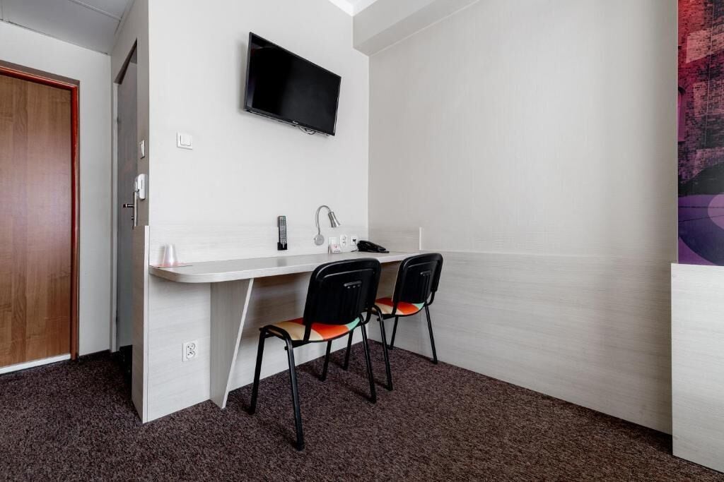 A small, modern room with a white desk, two black chairs, a mounted TV, and a door.