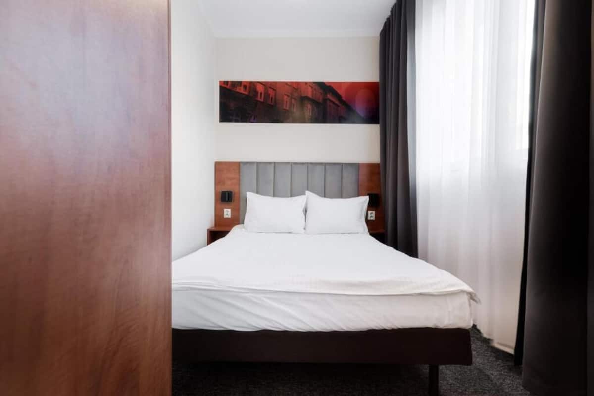 A hotel room with a bed, a headboard, a nightstand, and a painting on the wall.