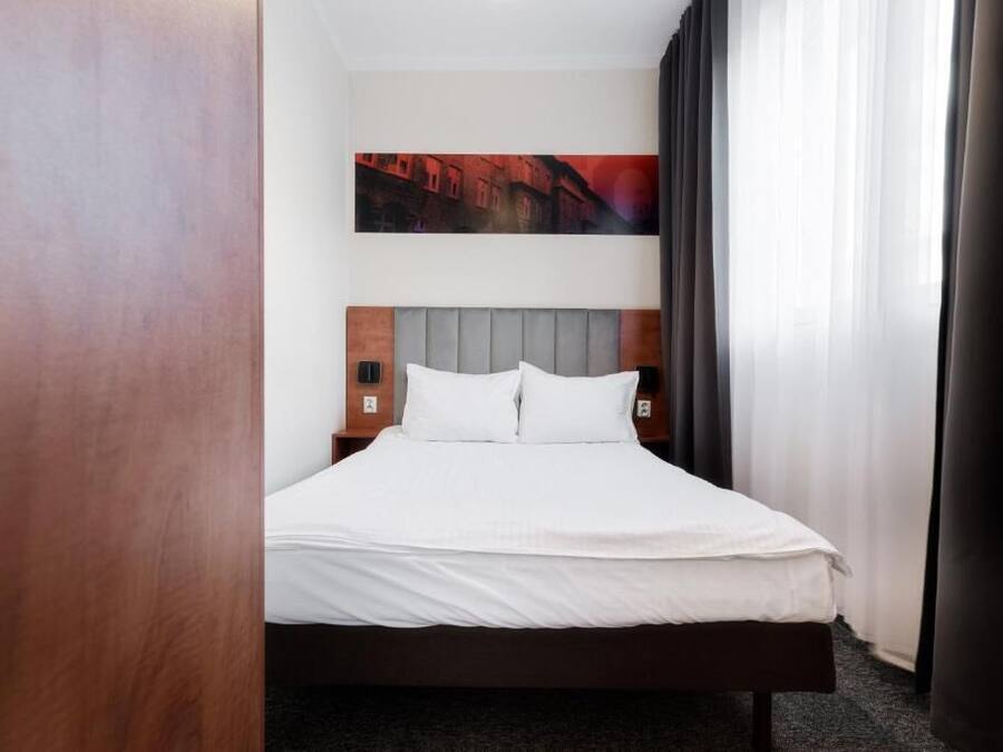 Habitación de hotel con una cama, cabecero, mesita de noche y un cuadro en la pared.