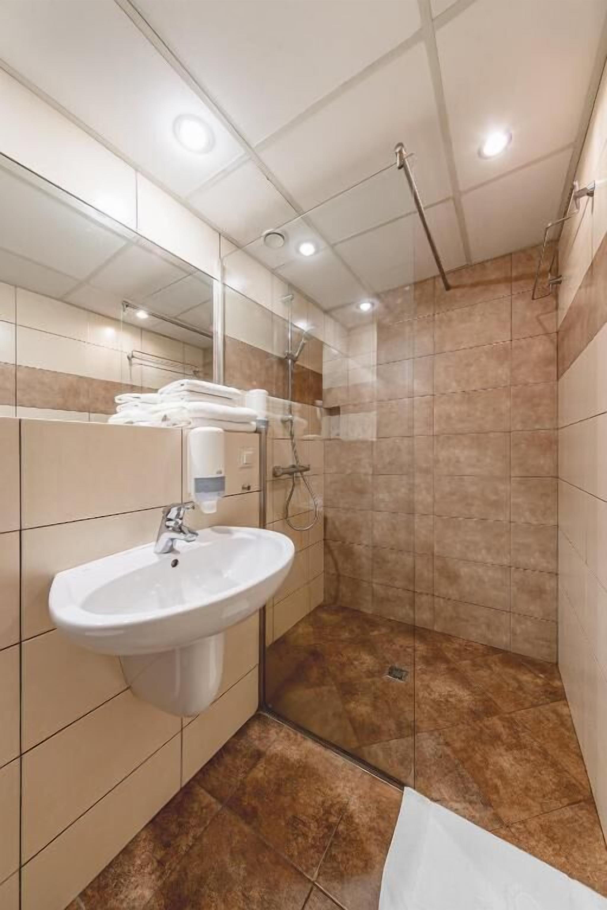 Un baño moderno con un lavamanos blanco, cabina de ducha con mampara de vidrio y paredes cubiertas de baldosas color beige.
