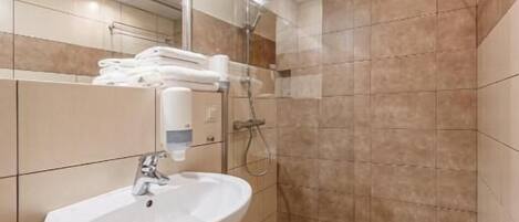 Un baño moderno con un lavamanos blanco, cabina de ducha con mampara de vidrio y paredes cubiertas de baldosas color beige.