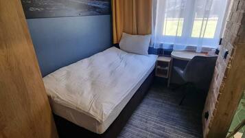 A compact room with a single bed, a small desk, and a window with curtains.