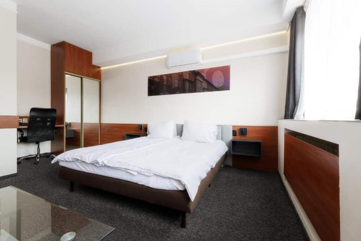 A hotel room with a bed, a desk, a chair, a wardrobe, and a wall-mounted air conditioner.