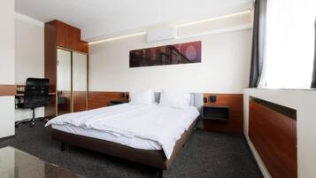 A hotel room with a bed, a desk, a chair, a wardrobe, and a wall-mounted air conditioner.