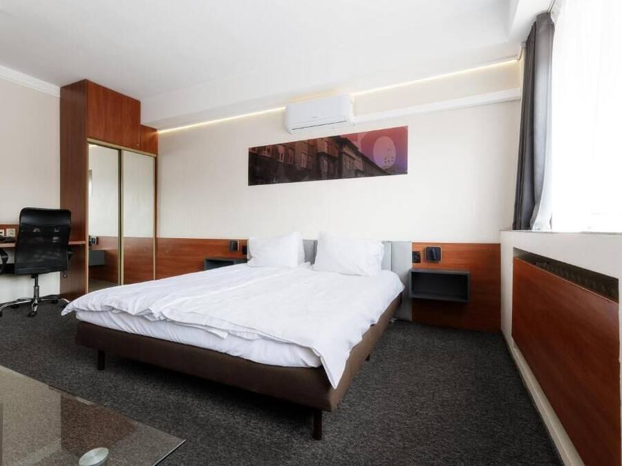 A hotel room with a bed, a desk, a chair, a wardrobe, and a wall-mounted air conditioner.