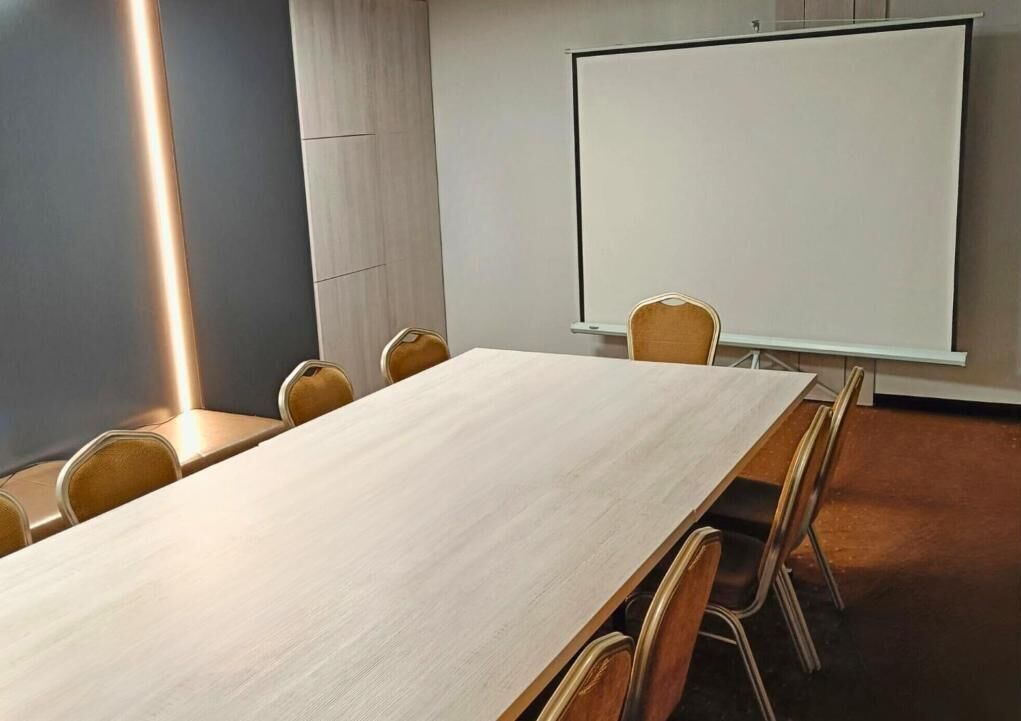 Una sala de conferencias con una larga mesa, seis sillas, una pizarra y una pantalla para proyector.