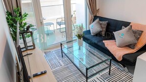 Un salon moderne avec une table basse en verre, un canapé agrémenté de coussins à motifs et une vue sur le balcon.