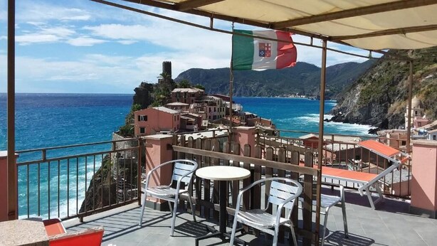 Terraza con mesas al aire libre, con vistas a un pueblo costero y al mar.