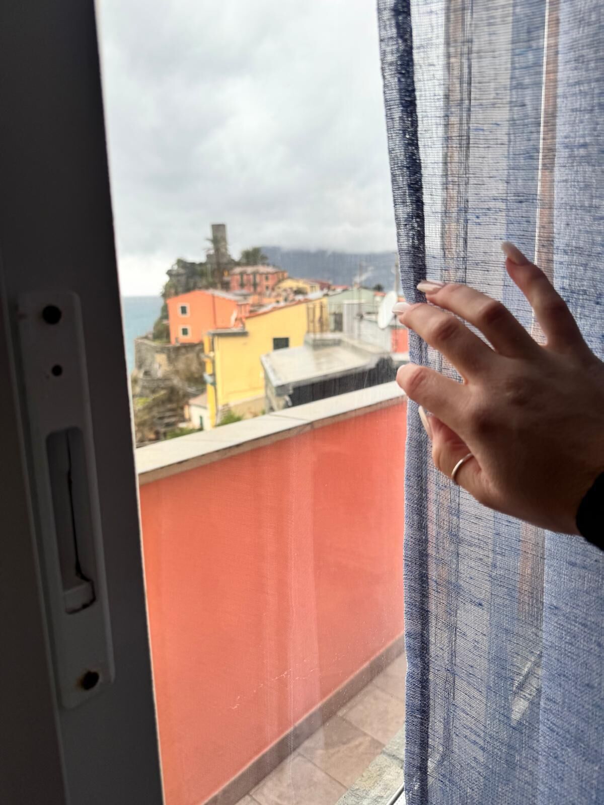 A hand on a window with a view of colorful buildings and a cliff.