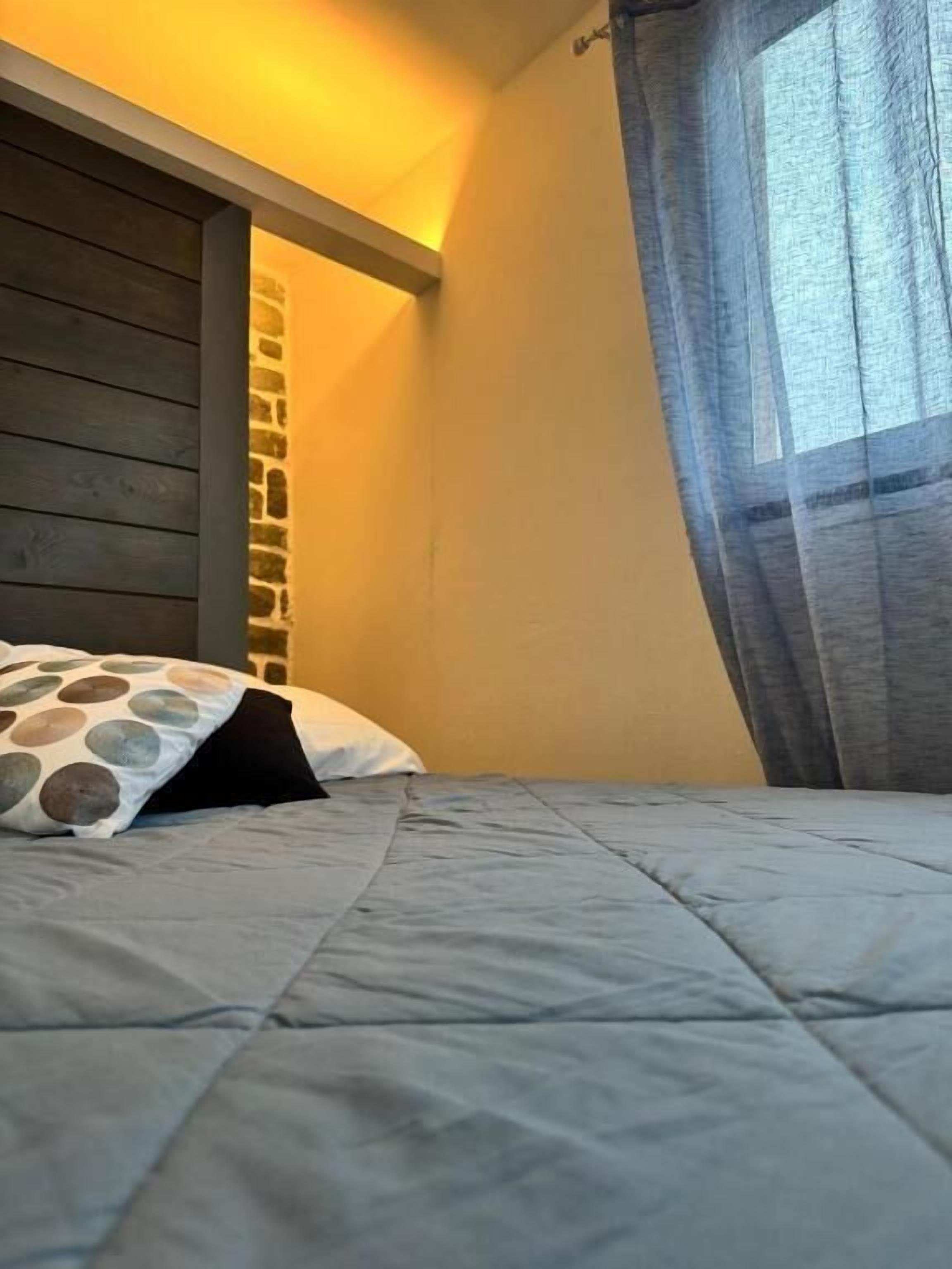 Un dormitorio con una cama, un almohadón, cabecera de madera y una ventana con cortinas.