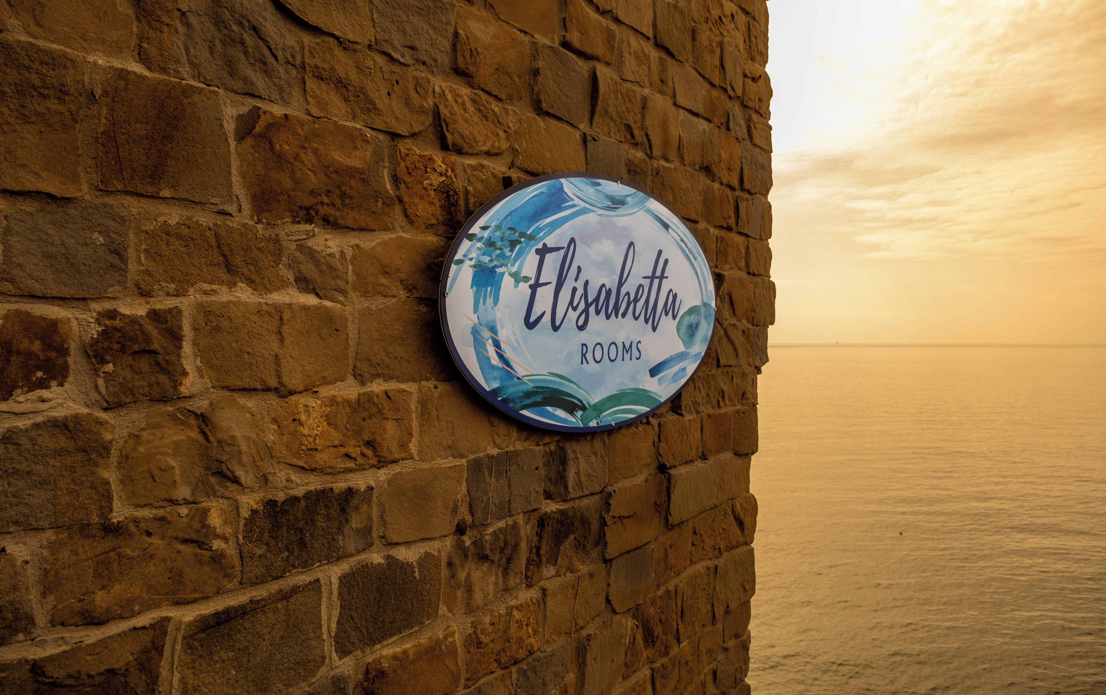 A brick wall with a circular sign that reads 'Elisabetta Rooms.'