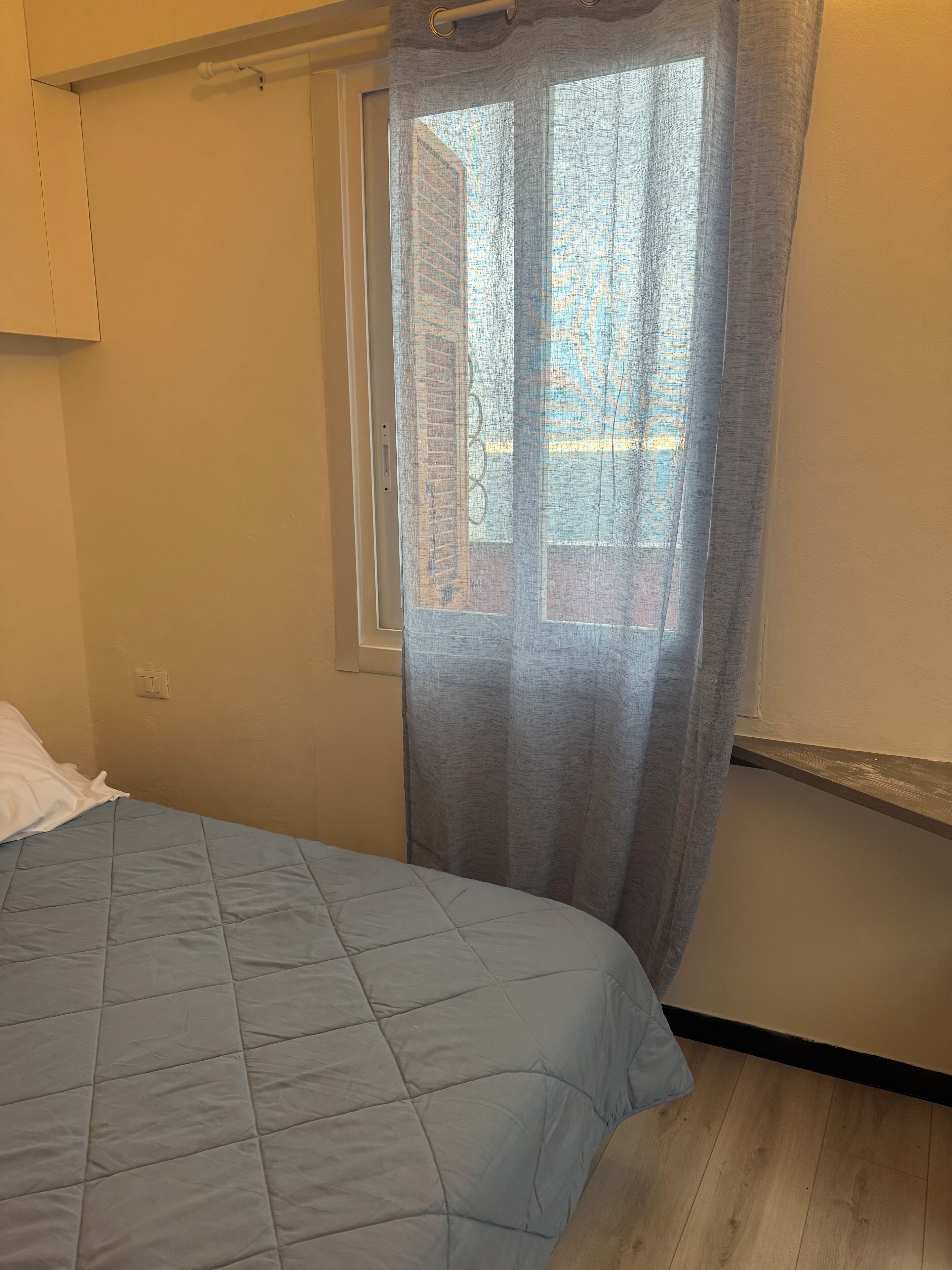 A bedroom with a bed, a window with a view of buildings, and a curtain.