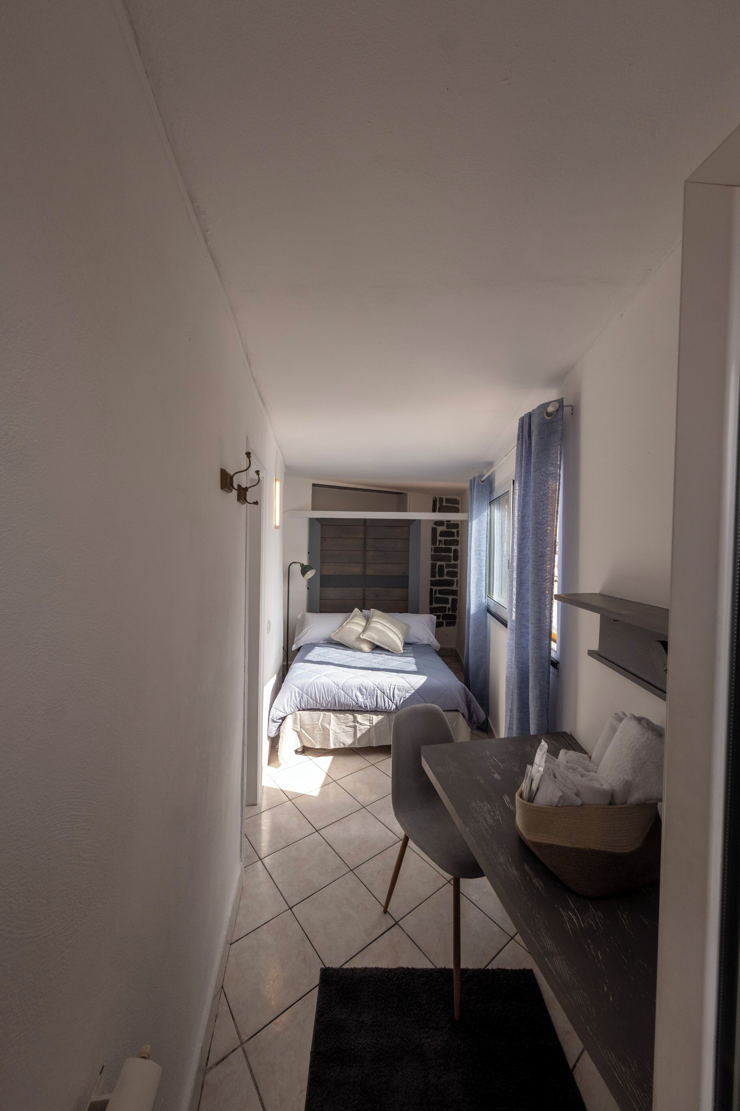 Un pasillo estrecho que da a un dormitorio con una cama, un escritorio y una silla.