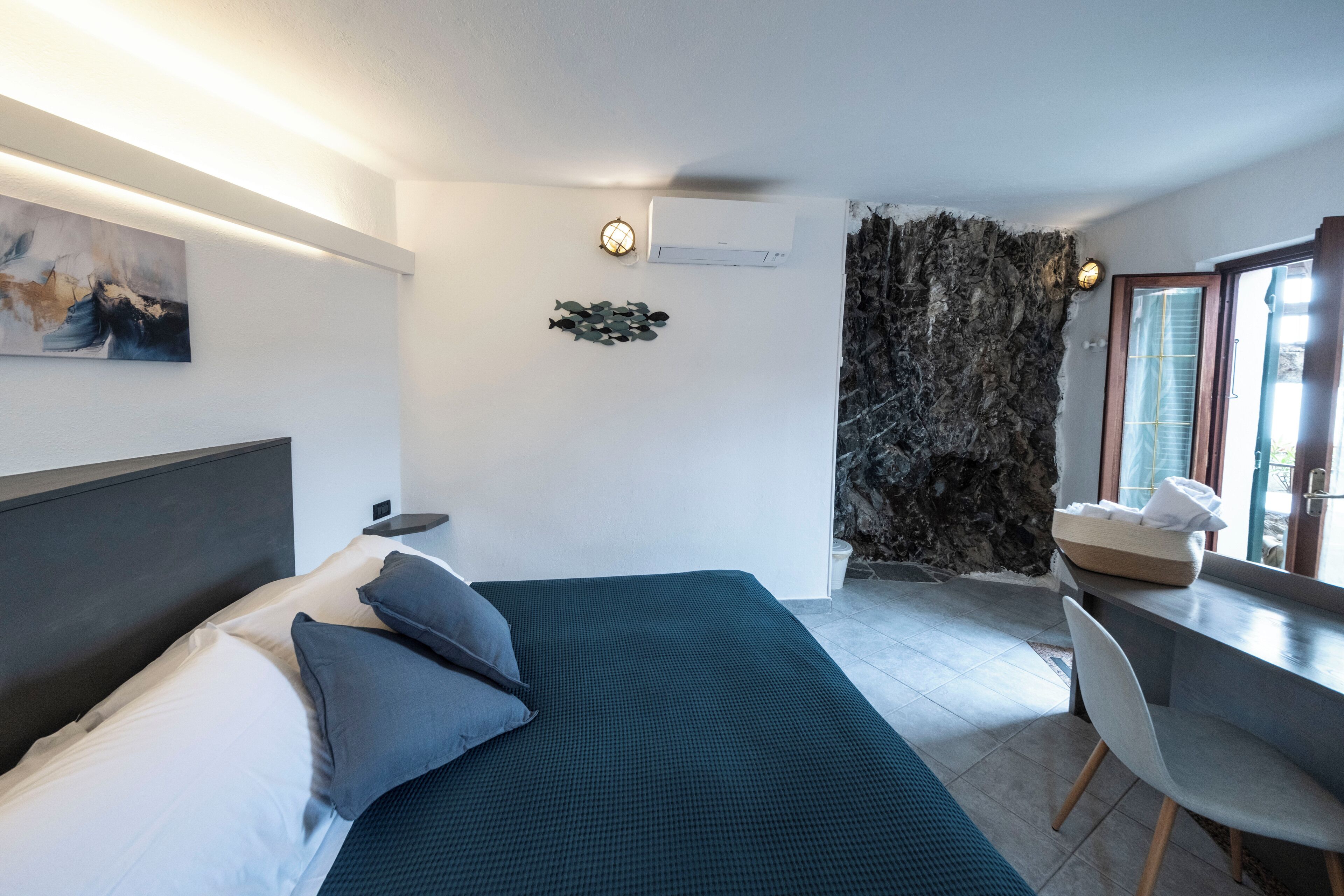 Una camera d'albergo moderna con un letto, una scrivania e un muro in pietra.
