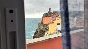 Vista costera con edificios en un acantilado, mar al fondo y una ventana con cortina que parcialmente cubre la vista.