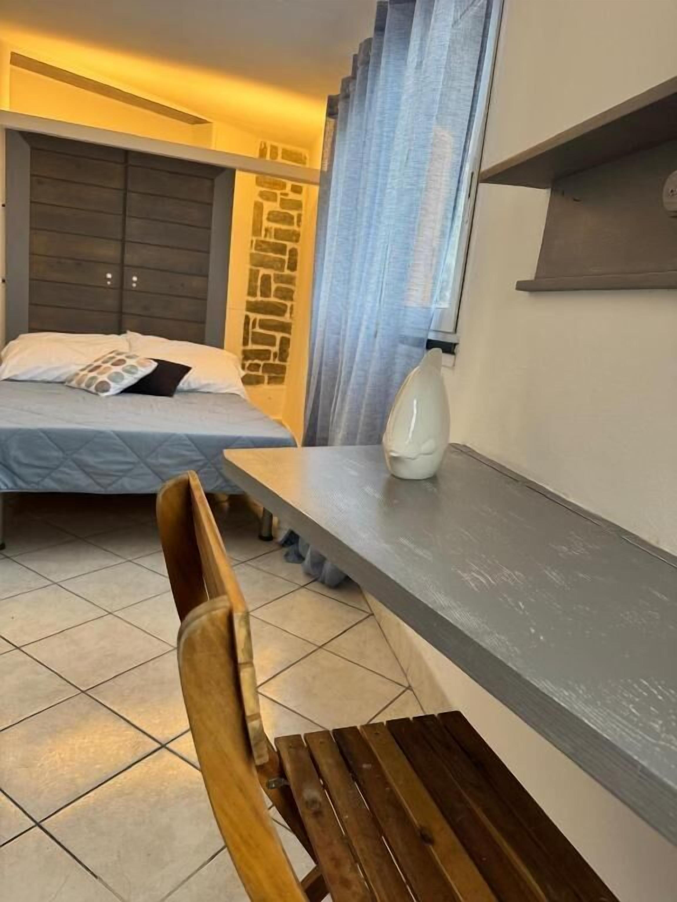 Un dormitorio con cama, mesita de noche, una silla y ventana con cortinas.
