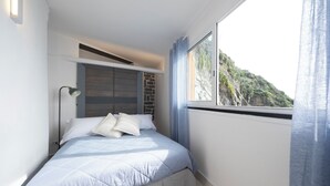 Un dormitorio con cama, mesita de noche, lámpara, ventana con cortinas y vista a un paisaje montañoso.