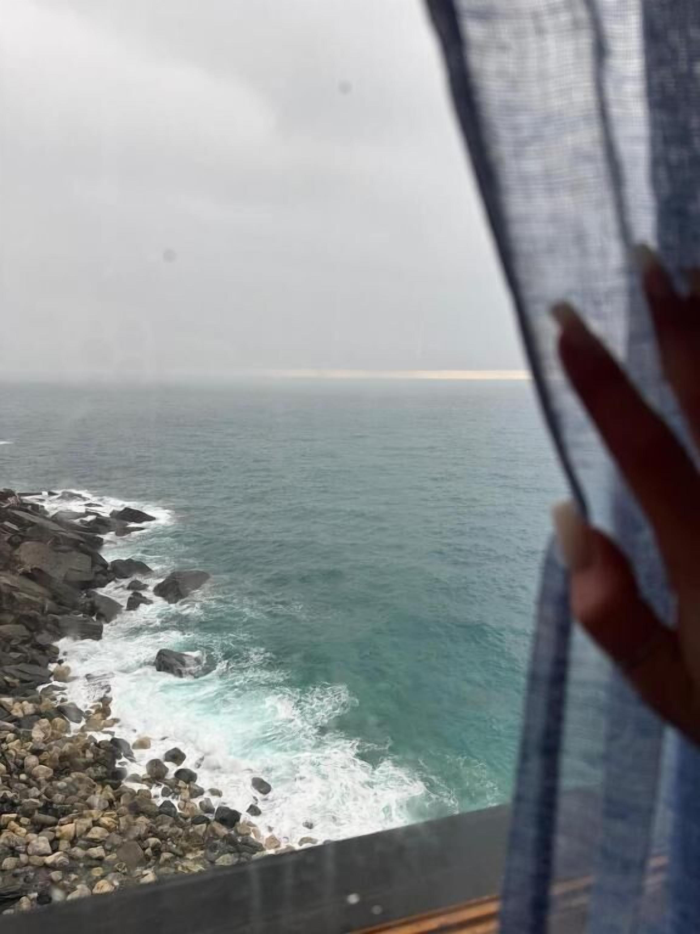 Vista del océano a través de una ventana, con una mano cubriendo parcialmente la escena.