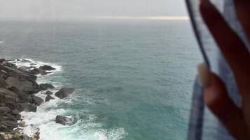 Vista del océano a través de una ventana, con una mano cubriendo parcialmente la escena.