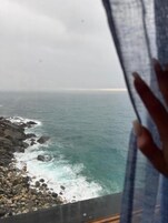 Vista del océano a través de una ventana, con una mano cubriendo parcialmente la escena.