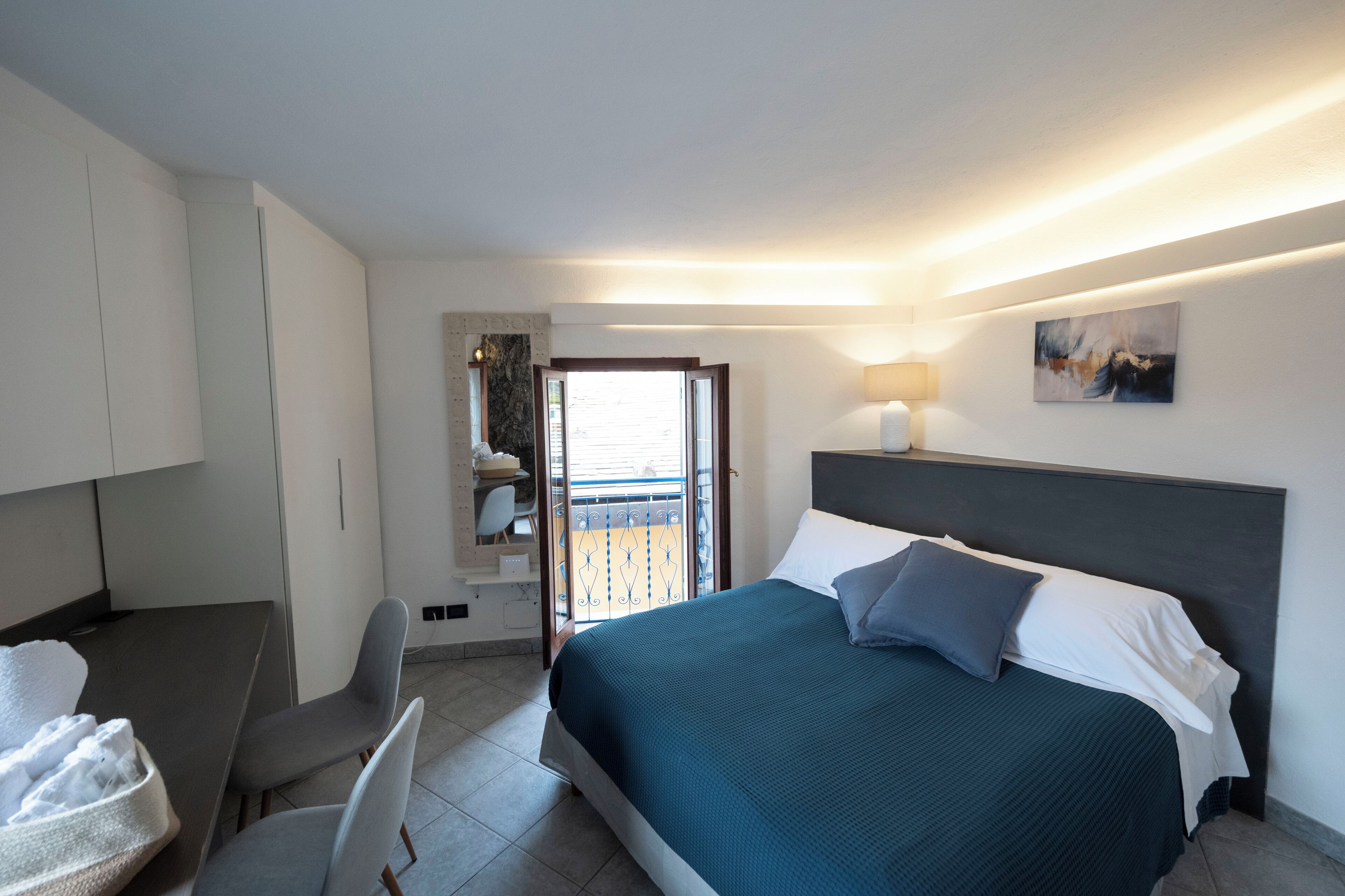 Une chambre d’hôtel avec un lit, un bureau, une chaise, un balcon et un tableau au mur.
