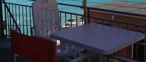 A balcony with a table and chairs, overlooking a clear blue sea.