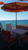 Un balcón con una mesa y sillas, con vista al mar azul y despejado.