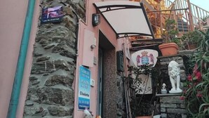 Un edificio con fachada de piedra, un muro rosa y un balcón con barandilla. Hay un cartel en la pared y una estatua en el suelo.