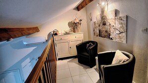 Une pièce avec un plafond en bois, une armoire blanche, une chaise noire et un mur orné d’un tableau représentant un Bouddha.