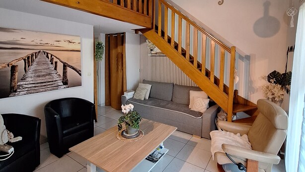Un vaste espace de vie comprenant un escalier en bois, un ensemble de canapés, une table à manger et une vue sur une terrasse en bois.