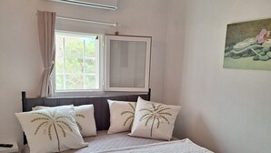 Une chambre à coucher avec un lit, des oreillers, une fenêtre, un climatiseur et un tableau accroché au mur.