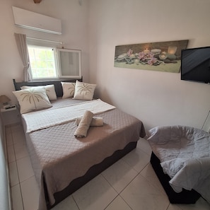 Une chambre Ă coucher avec un lit, une table de chevet, une lampe, une fenĂȘtre et un tableau au mur.