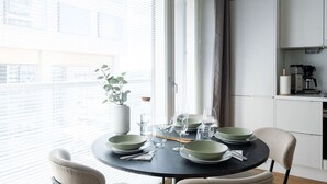 A dining area with a round table set for four, near a window with blinds.